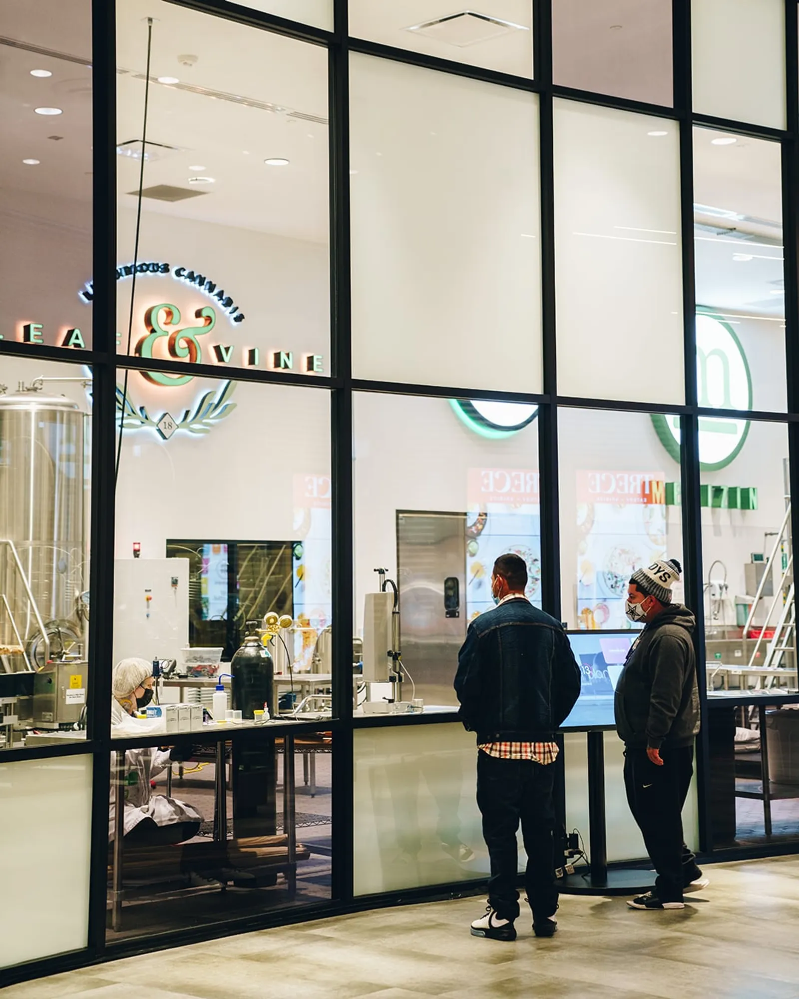 Two visitors watching a lab technician through the production floor window
