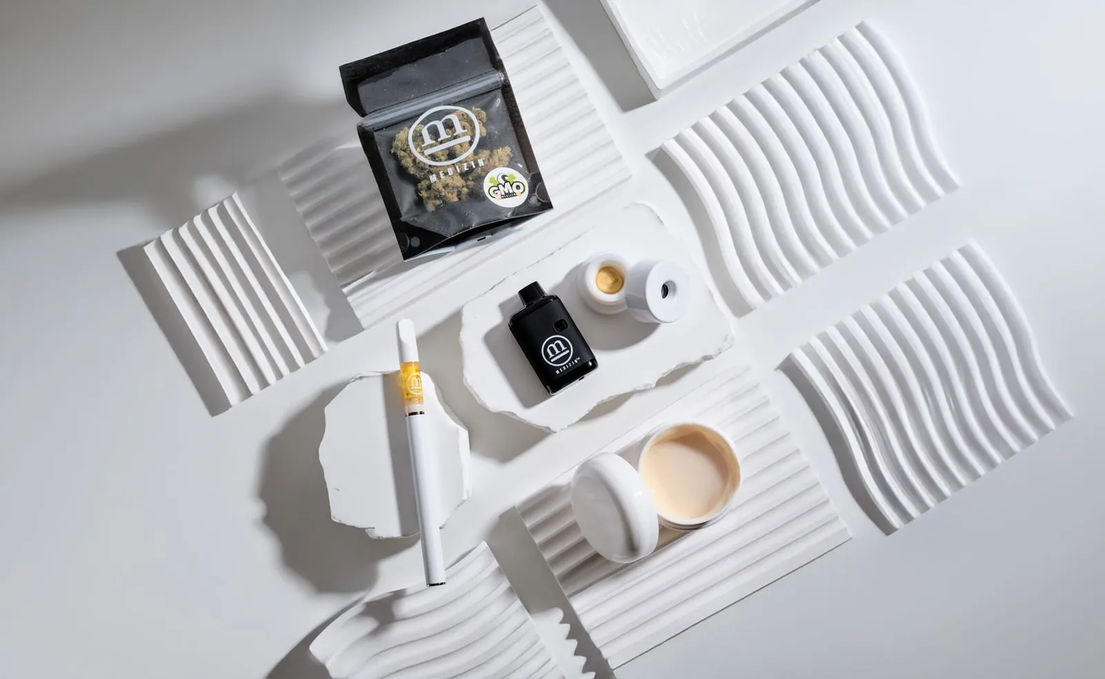 Medizin flower, a vape, concentrates and a cartridge laid out on white